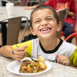 A photograph of a child smiling with a plate of food in front of them.